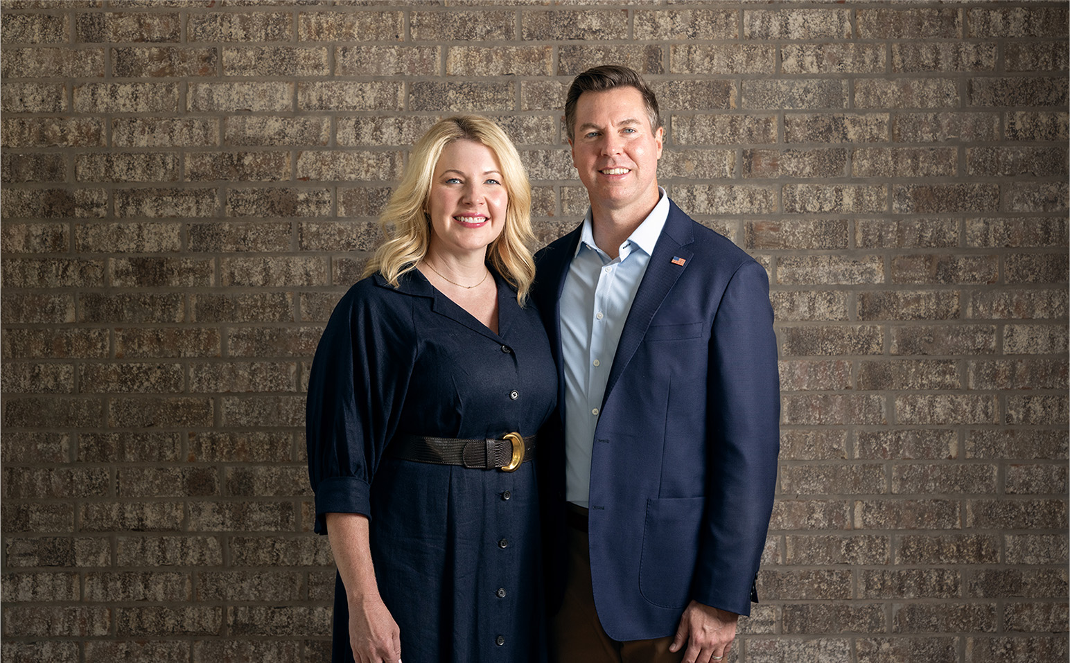 Adam Pugh and his wife posing in front of a brick wall