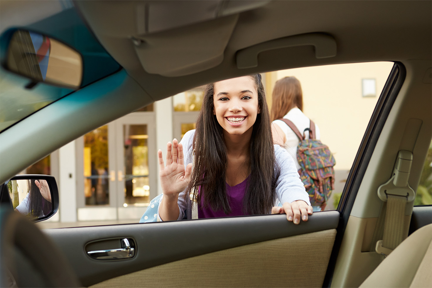 Young female student waving bye at school drop off